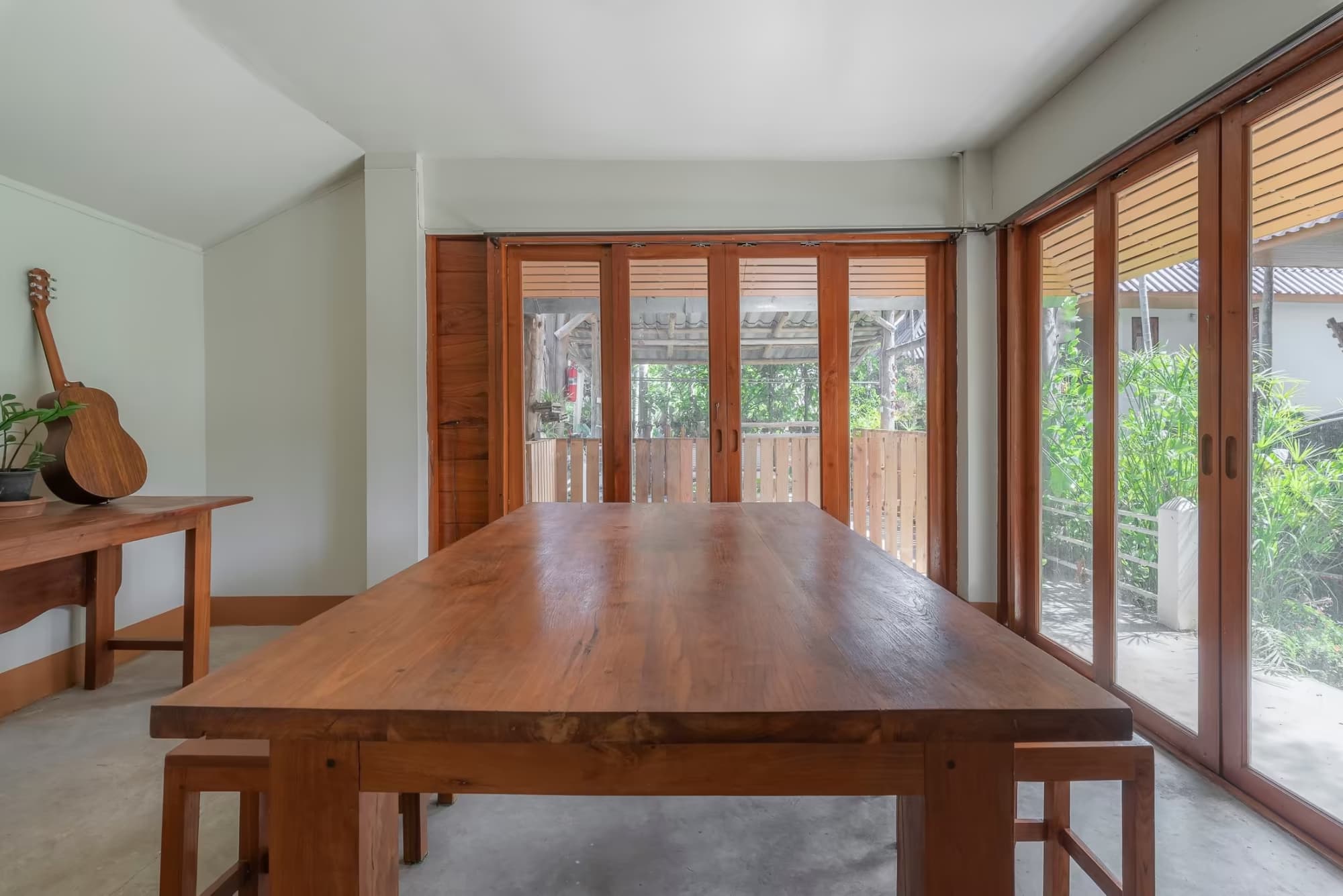 Betel Palm Village Pai indoor dining area with large solid-wood table, acoustic guitar and folding wood-and-glass doors opening to greenery