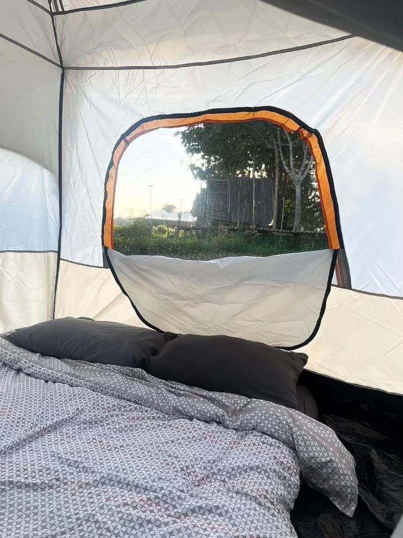 Inside the tent at Camp View Mountain, Pai — futon bed with pillows beside an open mesh window looking out to the rice field at golden hour