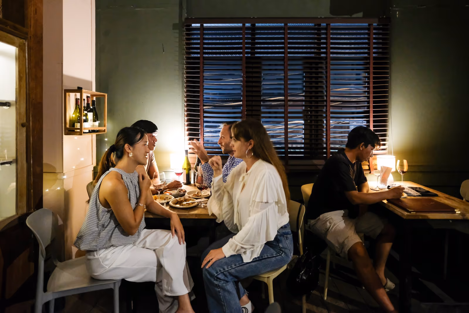 Friends at dinner by the window at Vermut Café, Pai — small plates and wine under a table lamp