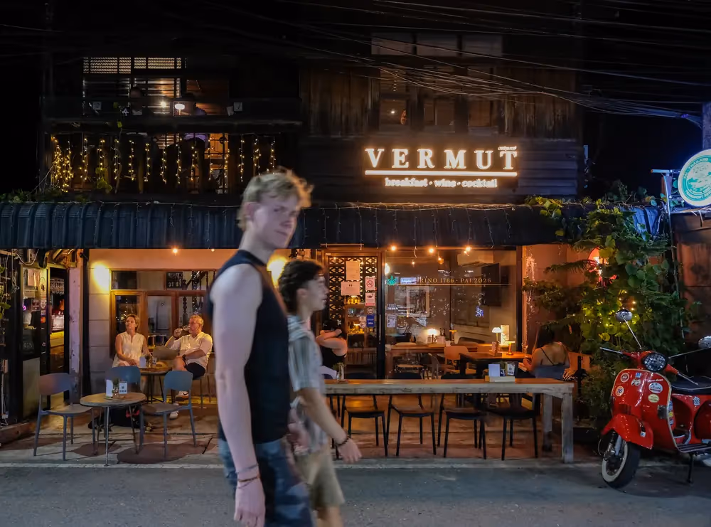 The lit VERMUT sign at night on Pai Walking Street, a couple walking past the open front